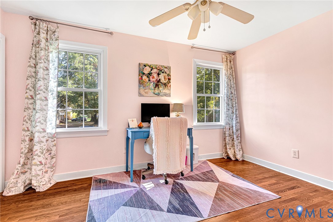 Room featuring wood-finish flooring, two double-hung windows, and a ceiling fan with integrated lighting