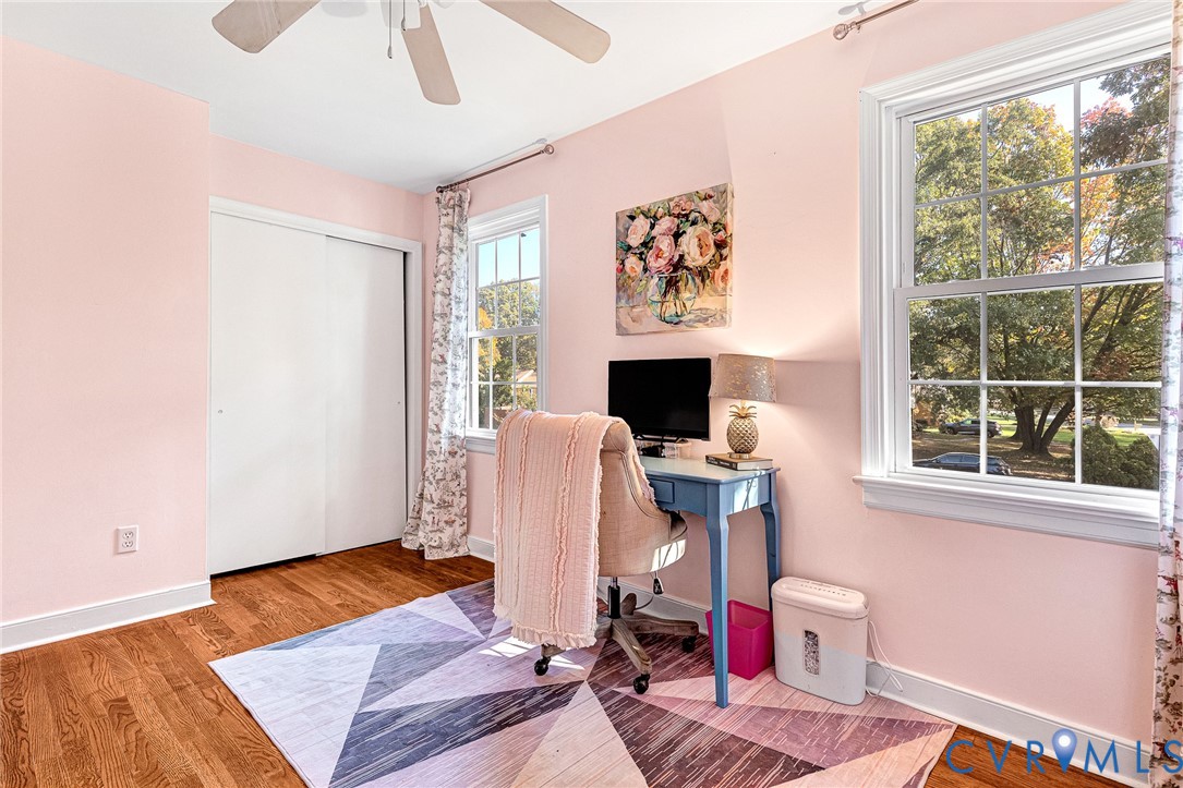 Room featuring wood-finish flooring, dual windows with white casing, sliding-door closet, and a ceiling fan with light fixture