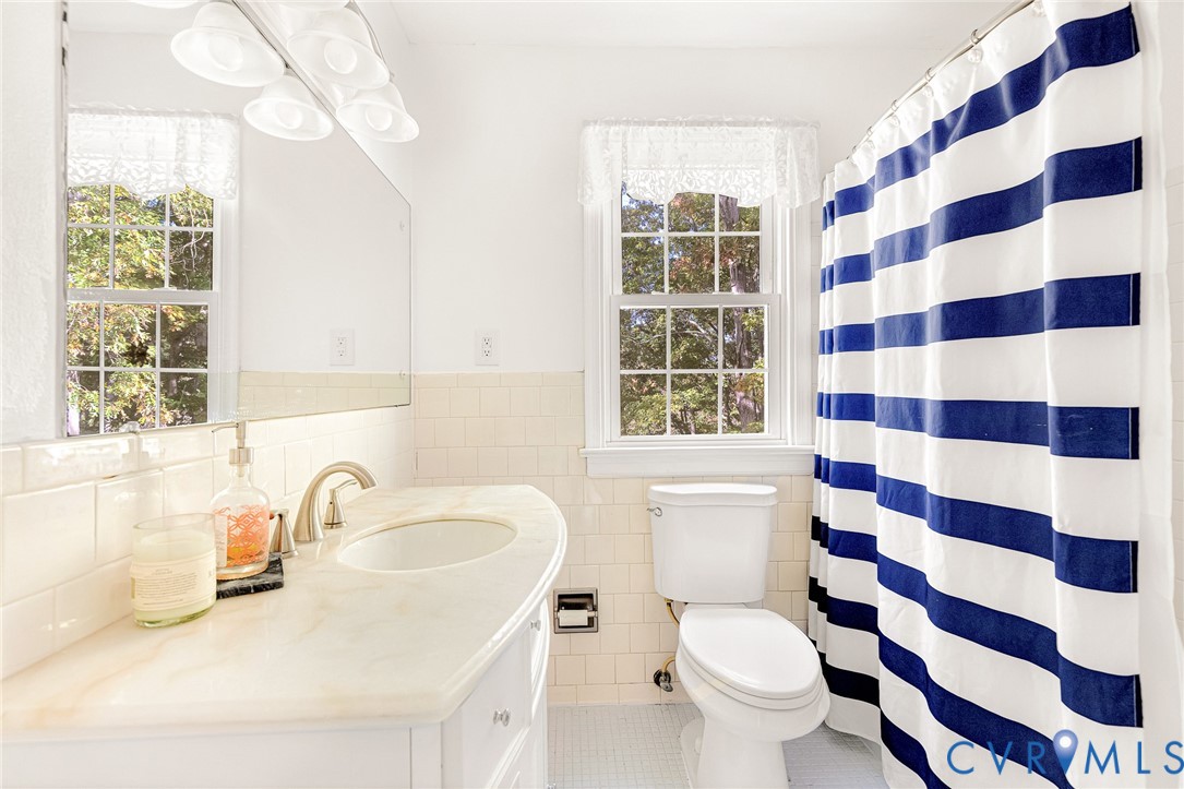 Vanity with a solid surface countertop, integrated sink, polished metal faucet, subway tile wainscoting, and large wall-mounted mirror