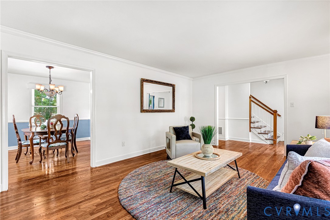 Living area featuring wood-finish flooring, crown molding, a decorative chair rail, and an open entryway with a wood-accented staircase