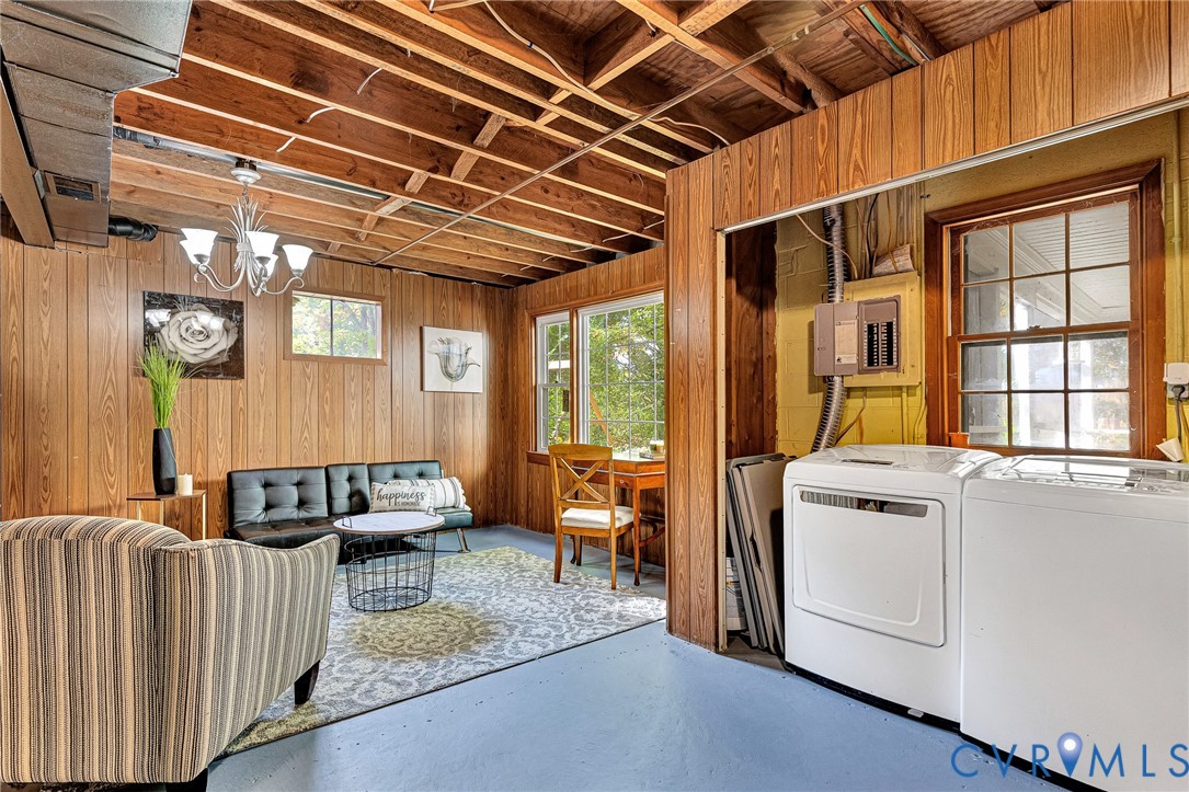 Multi-purpose space featuring wood-paneled walls, exposed ceiling joists, multi-pane windows, and a dedicated laundry area with electrical panel access