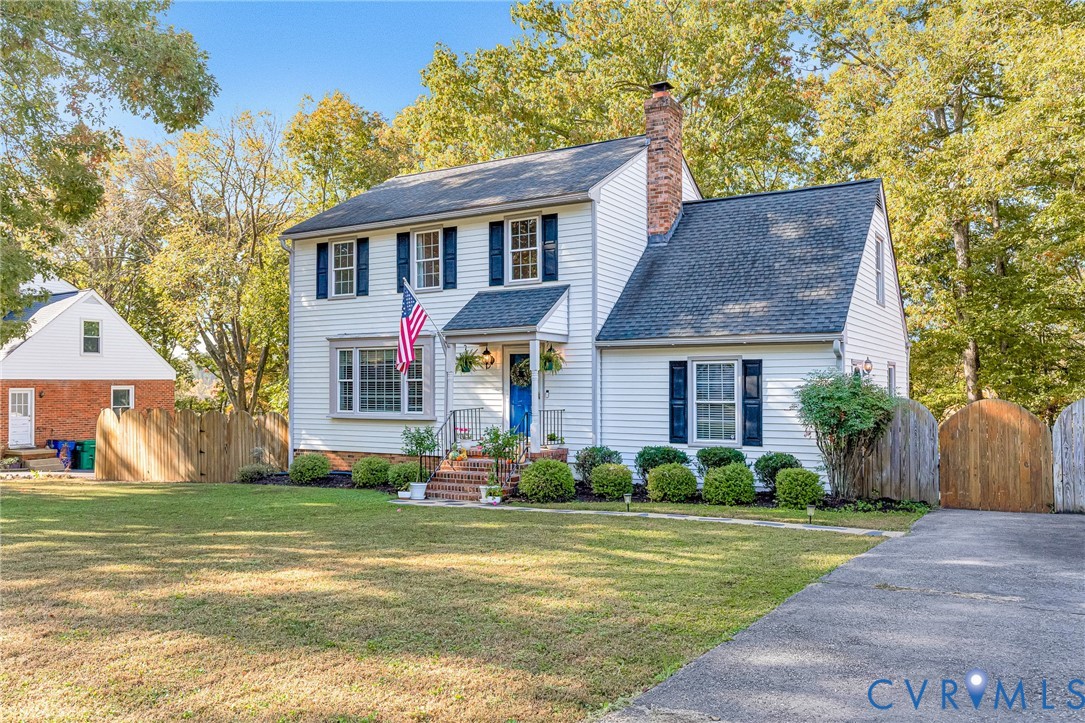 Colonial-style exterior featuring white horizontal siding, dark blue shutters, a central brick chimney, a covered front entry with brick steps, and a multi-level asphalt shingle roof