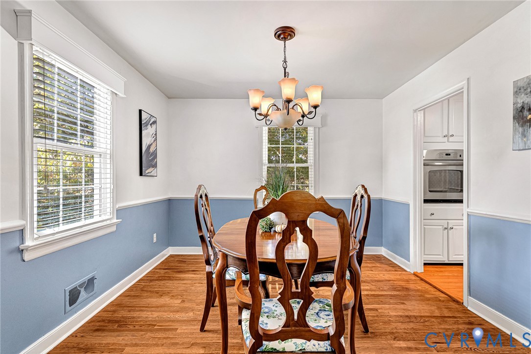 Dining area featuring wood-finish flooring, two-tone wall paint with chair rail molding, multi-light chandelier, and double-hung windows