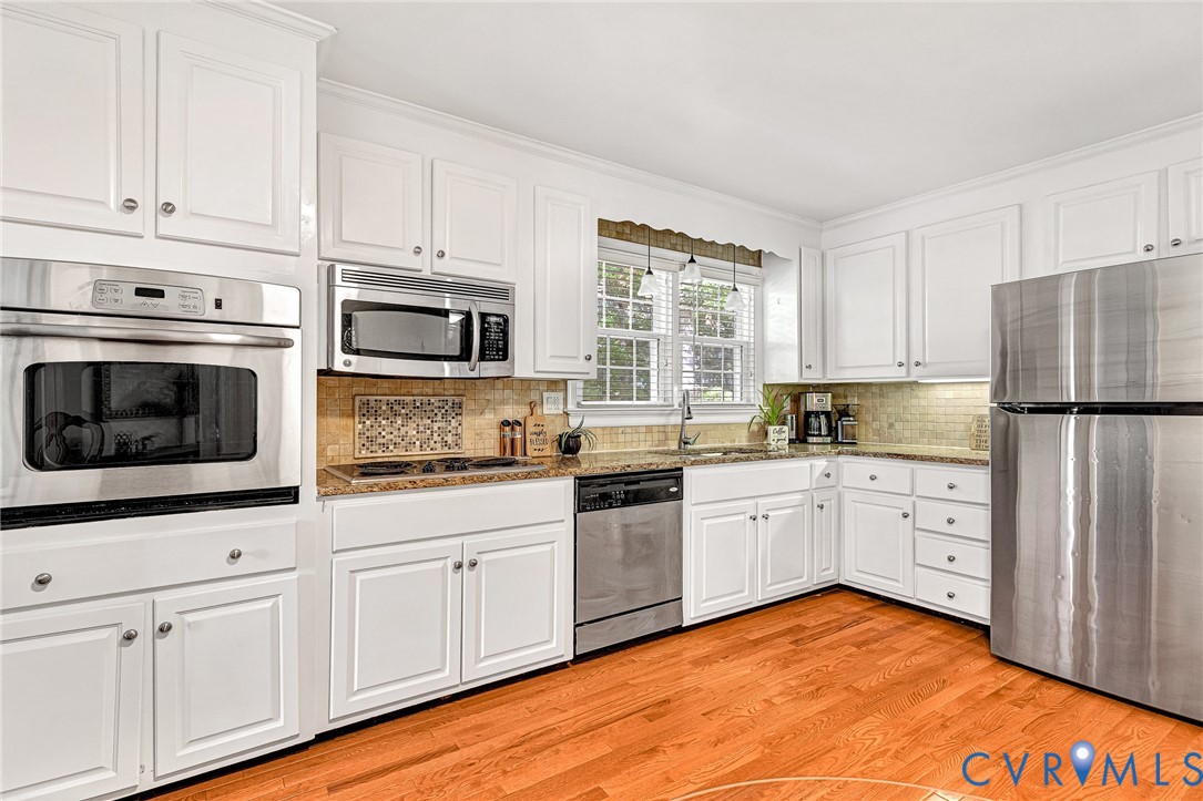 Kitchen featuring white cabinetry, stone-finish countertops, stainless steel appliances, wood-finish flooring, and a decorative tile backsplash