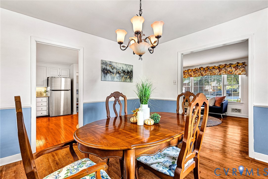 Dining area featuring wood-finish flooring, a decorative chandelier, and chair rail molding