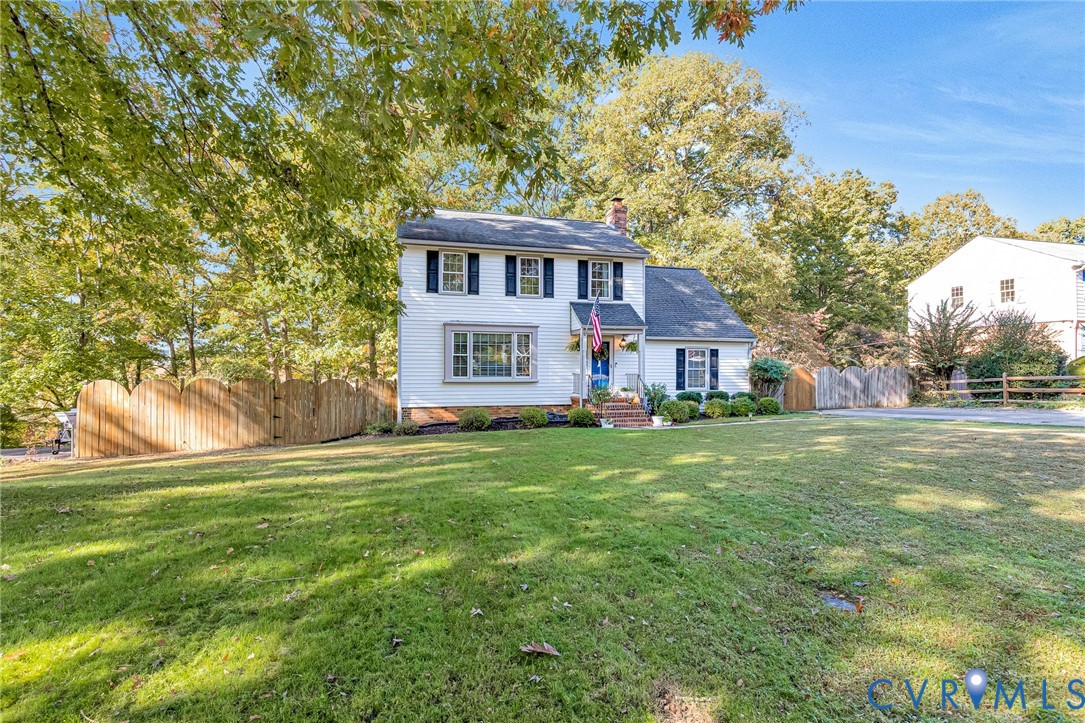 Two-story traditional exterior featuring white lap siding, dark shutters, a front gabled entryway, a masonry chimney, and a picket-style wood privacy fence