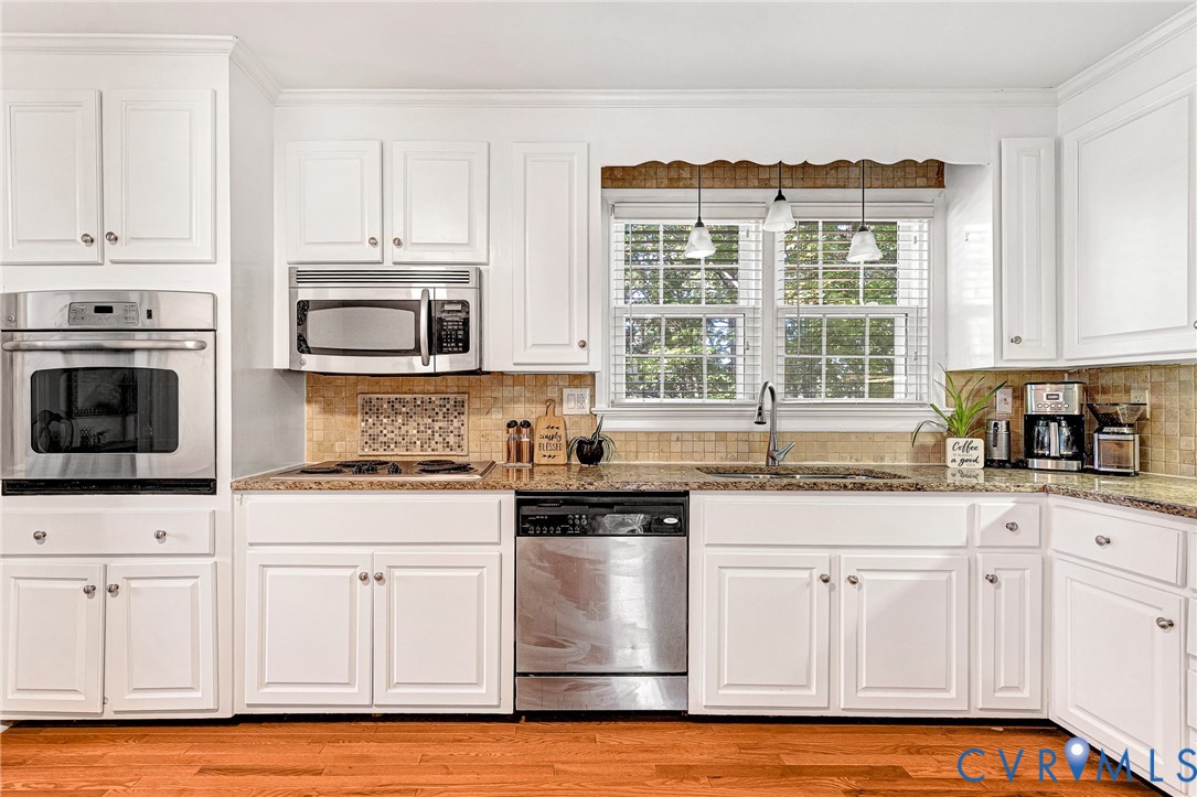 Kitchen featuring white cabinetry, stone countertops, stainless steel appliances including a built-in wall oven and microwave, stone tile backsplash, and wood-finish flooring