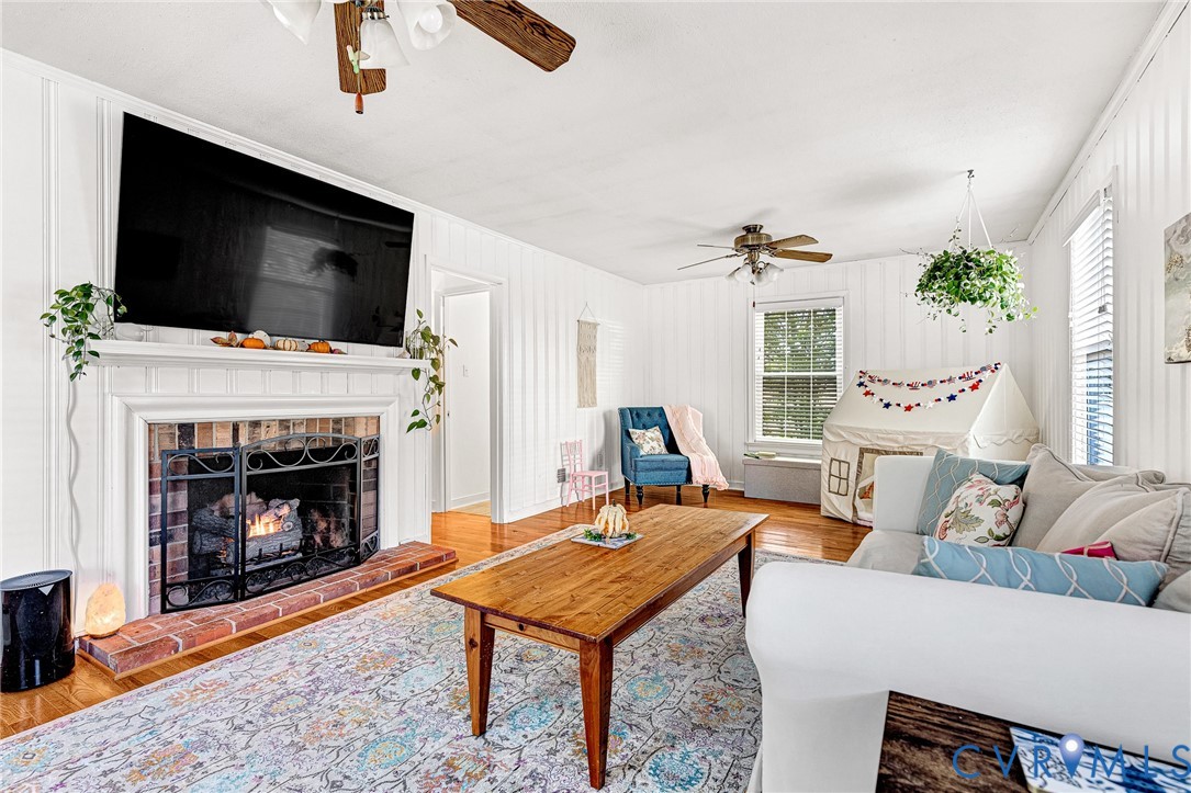 Living space featuring wood-finish flooring, vertical panel wall detailing, and a brick-surround fireplace with a classic white mantel