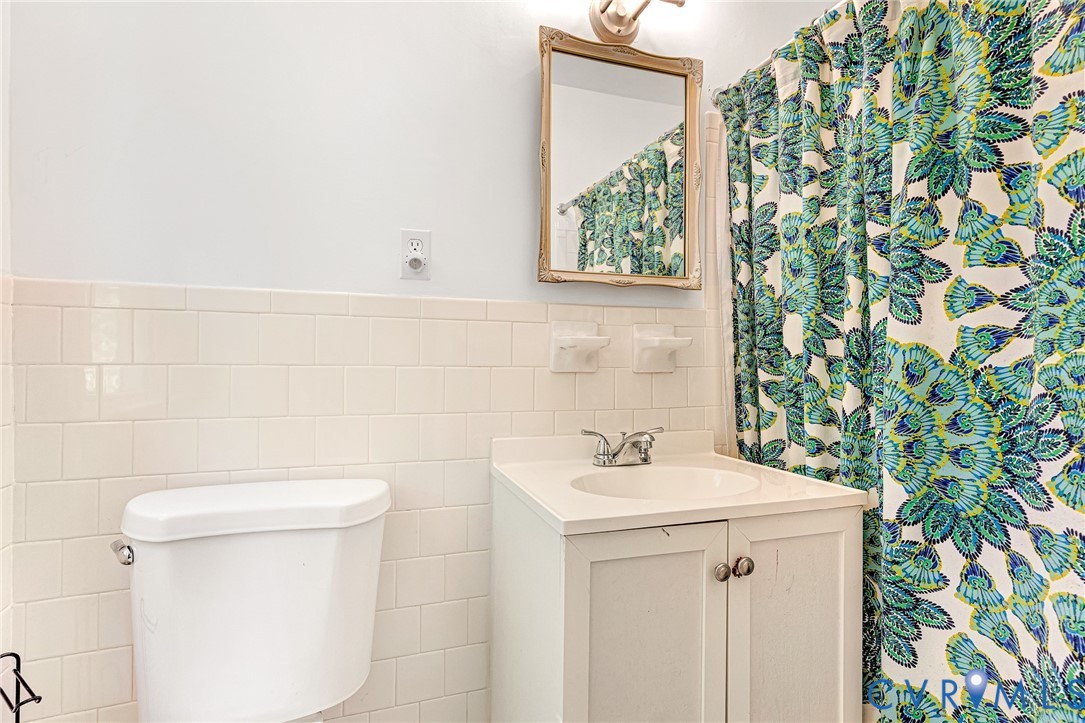 Bathroom featuring white subway tile wall wainscoting, a white vanity cabinet with an integrated countertop sink, a dual-handle faucet, and an attached wall-mounted mirror