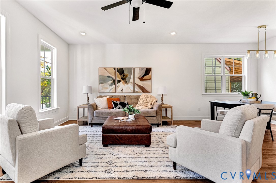 Open-concept interior featuring wood-finish flooring, recessed lighting, a matte black ceiling fan, and multi-light brushed gold chandelier