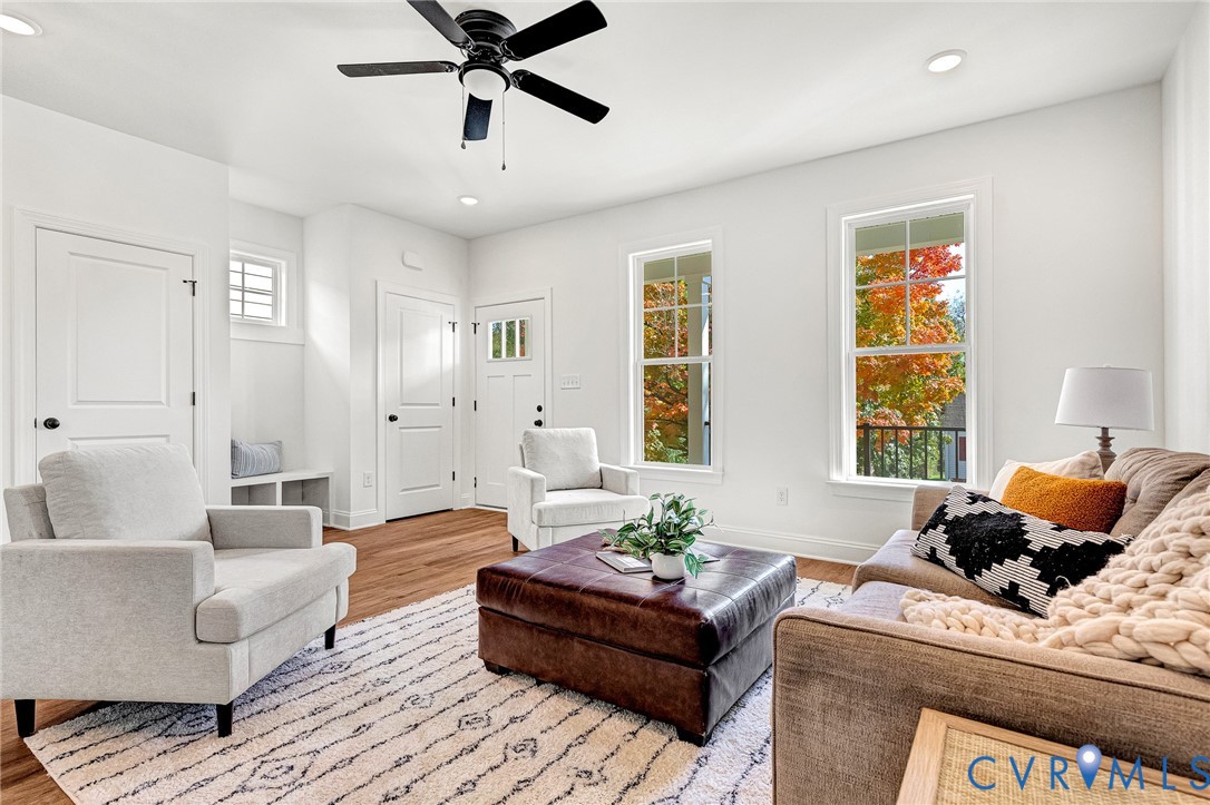 Living area featuring wood-finish flooring, two full-height windows, a ceiling fan, and built-in cabinetry