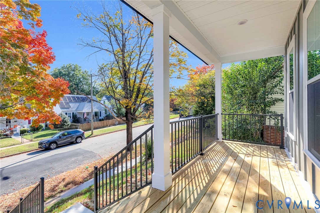 Covered front porch featuring wood decking, black metal railings, and square support columns with recessed ceiling lighting