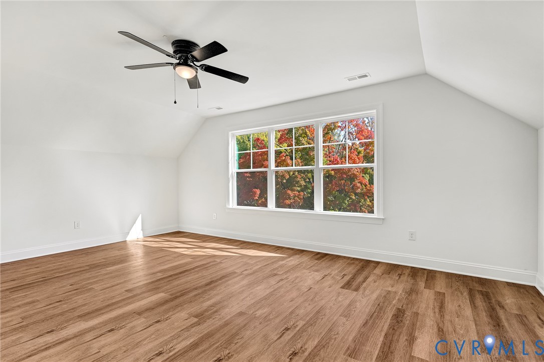 Vaulted ceiling with a matte black ceiling fan, wood-finish flooring, and large paneled windows