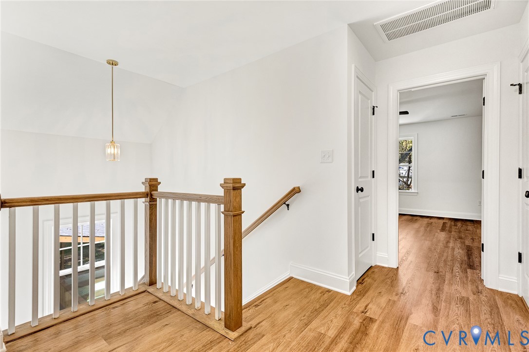 Landing featuring wood-finish flooring, a wood and white spindle balustrade, a singular brass-toned pendant light, and interior doors with black hardware