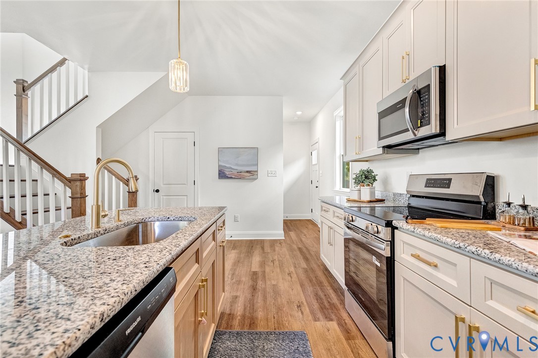 Kitchen featuring light-toned shaker cabinetry, stone-finish countertops, stainless steel appliances, a brass-finish faucet, and wood-finish flooring