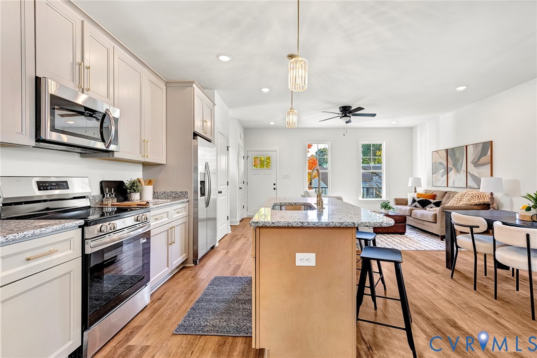 Kitchen featuring stone countertops, stainless steel appliances, a central island with bar seating, cabinetry with modern hardware, and wood-finish flooring