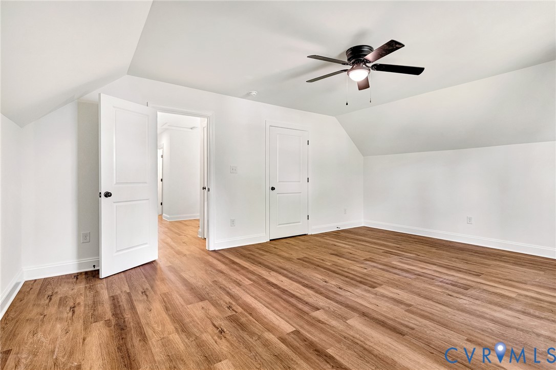 Room featuring wood-finish flooring, vaulted ceilings, and a central ceiling fan with an integrated light fixture