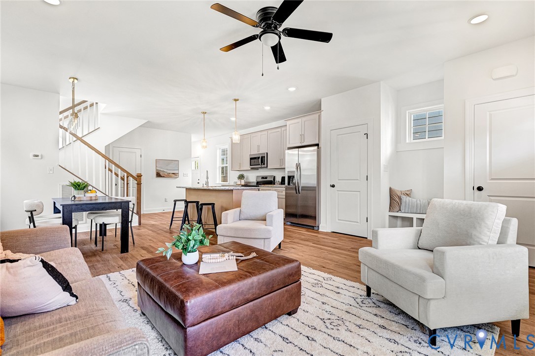 Open-concept interior featuring wood-finish flooring, a kitchen with stainless steel appliances, a center island with pendant lighting, a recessed staircase with a wooden handrail, and built-in bench seating