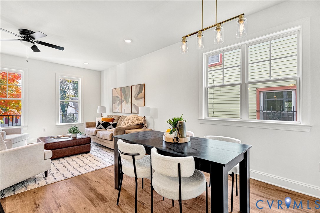 Open-concept room featuring wood-finish flooring, multi-pane windows, recessed ceiling lighting, a matte black ceiling fan, and a four-light linear pendant fixture