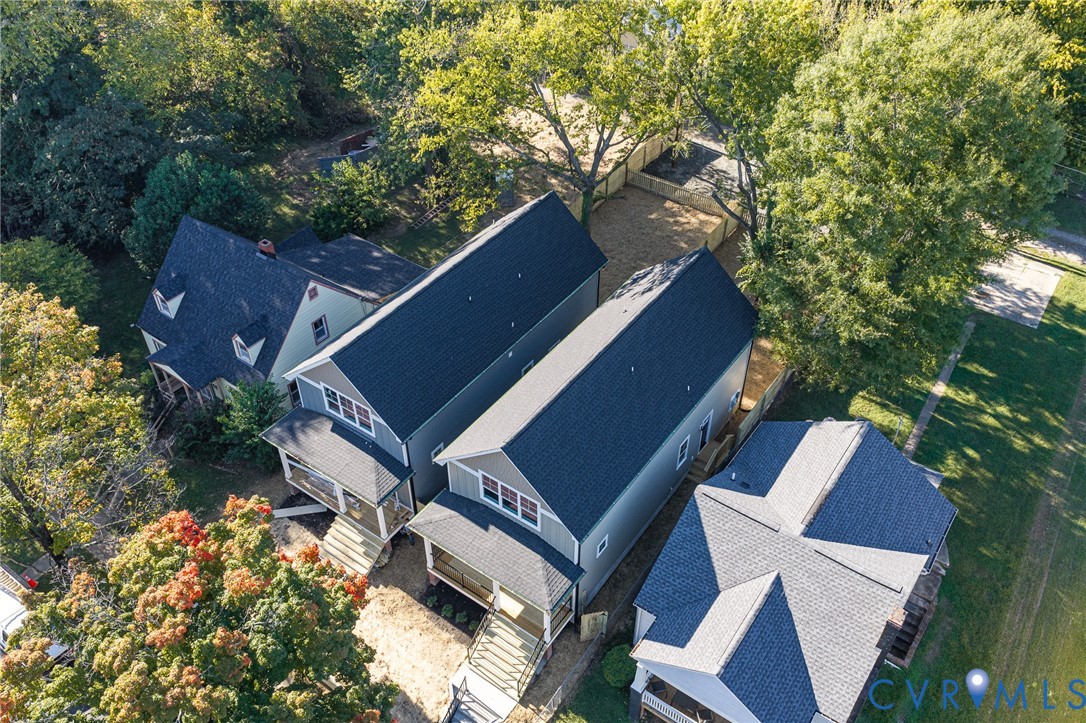 Aerial perspective of modern residential structures featuring gable rooflines, neutral siding, covered front porches with metal railings, and mature surrounding trees