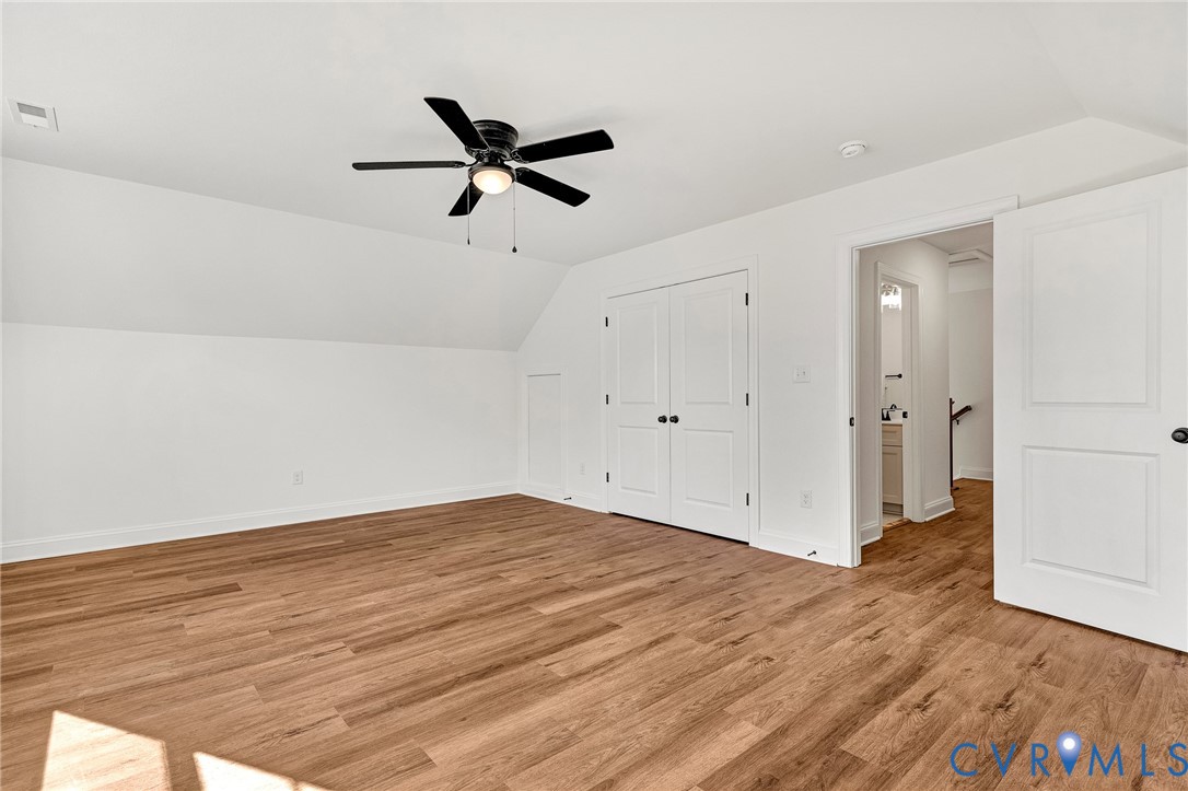 Room featuring wood-finish flooring, a matte black ceiling fan with integrated lighting, slanted ceilings, double-panel interior doors, and a reach-in closet