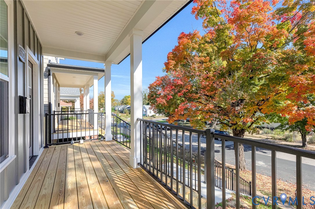 Covered front porch featuring wood-plank flooring, white structural columns, and black metal railings