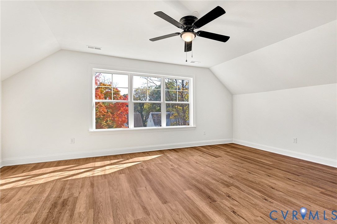 Vaulted ceilings, wood-finish flooring, multi-pane window, and a central ceiling fan with integrated lighting