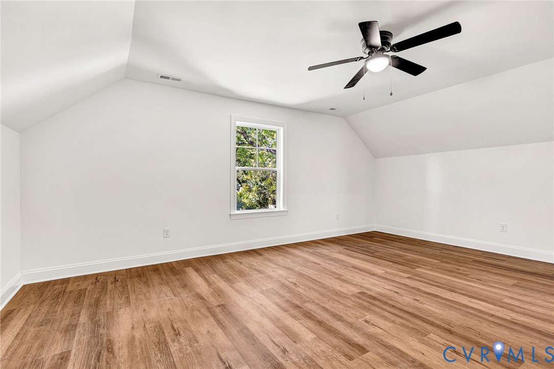 Sloped ceilings, wood-finish flooring, a single-hung window with a grille pattern, and an overhead ceiling fan with integrated lighting