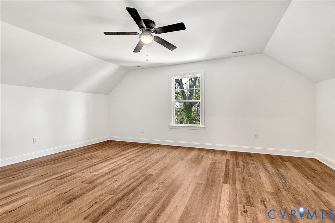 Room with slanted ceilings, wood-finish flooring, a central ceiling fan with an integrated light fixture, and a single-pane window