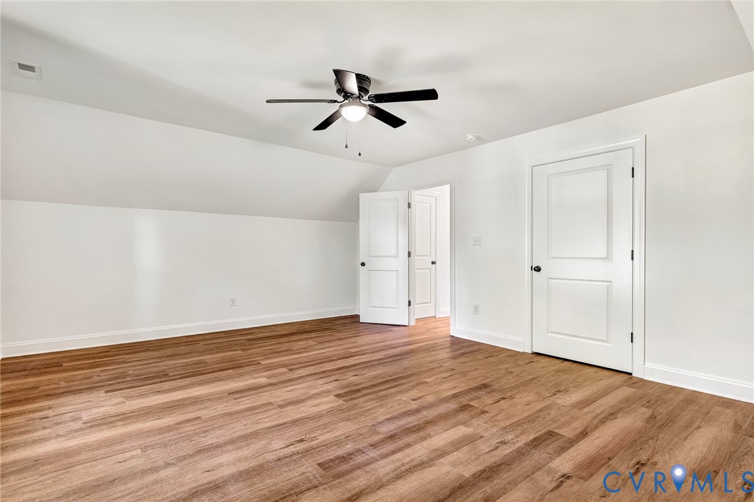 Room interior featuring wood-finish flooring, vaulted ceiling, dual-panel interior doors, and a central ceiling fan with integrated light