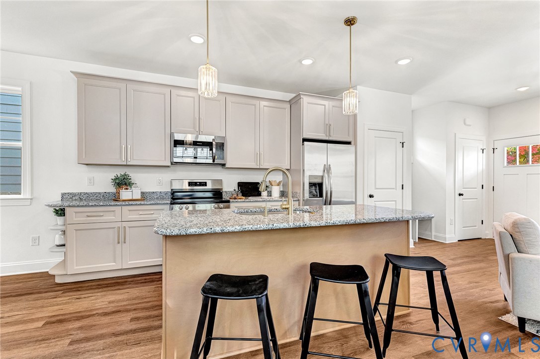Kitchen featuring cabinetry with brushed nickel hardware, stone-composite countertops, stainless steel appliances, a center island with a faucet, and wood-finish flooring