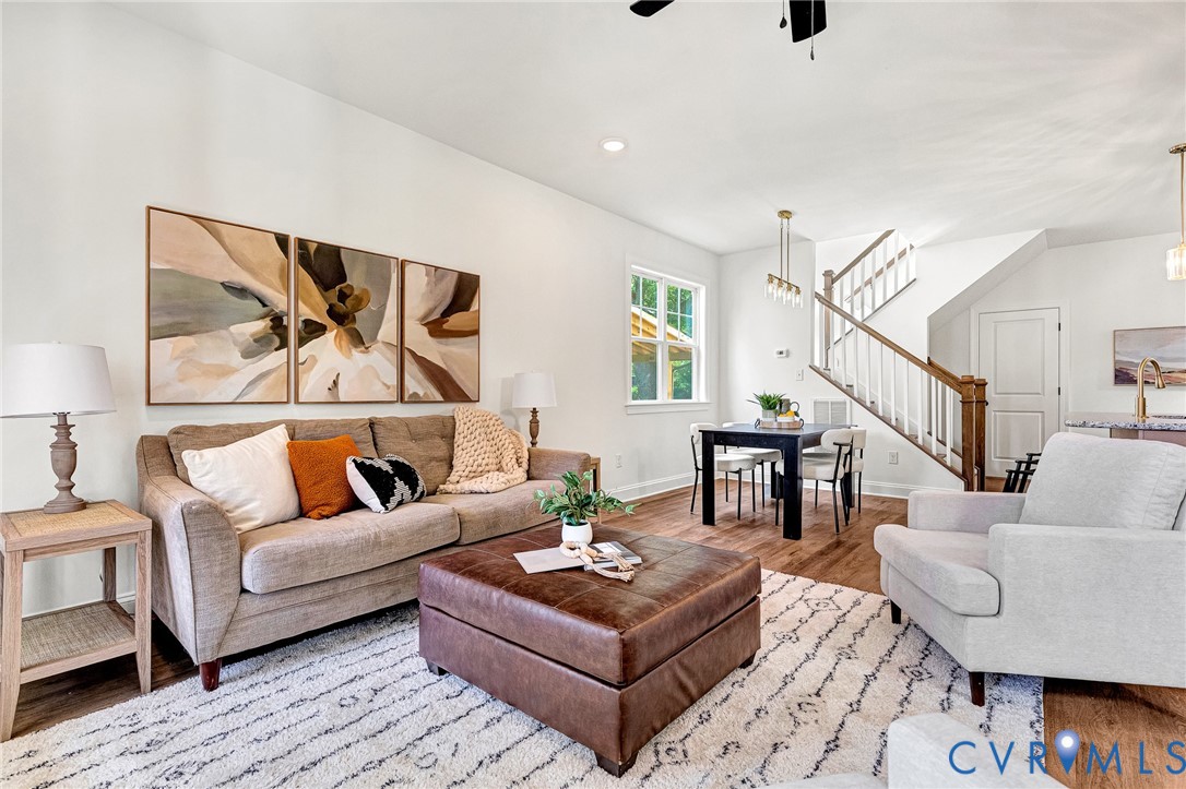 Living area featuring wood-finish flooring, recessed lighting, and a staircase with a stained wood handrail and white balusters