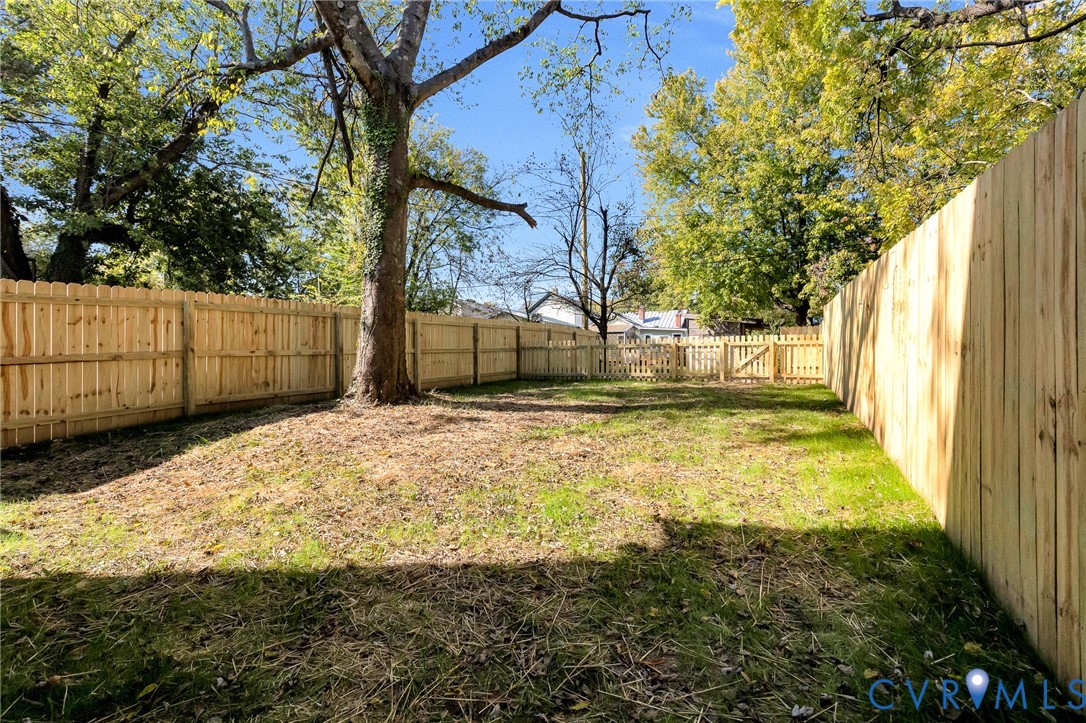 Fenced backyard featuring wood privacy fencing, a gate, mature trees, and grass lawn