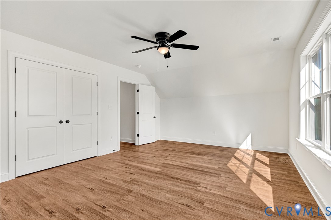 Wood-finish flooring, white double-panel closet doors, and a ceiling fan with integrated lighting