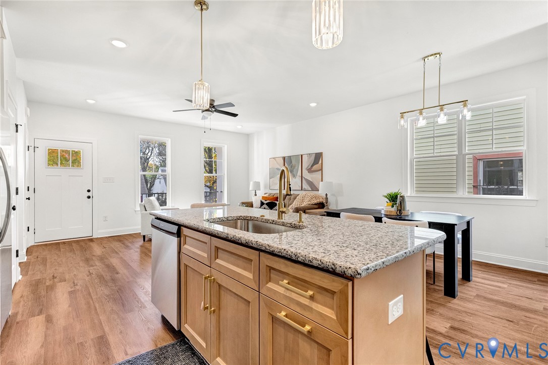 Kitchen island with stone countertop, undermount sink, and metallic faucet, complemented by wood-finish flooring and pendant lighting