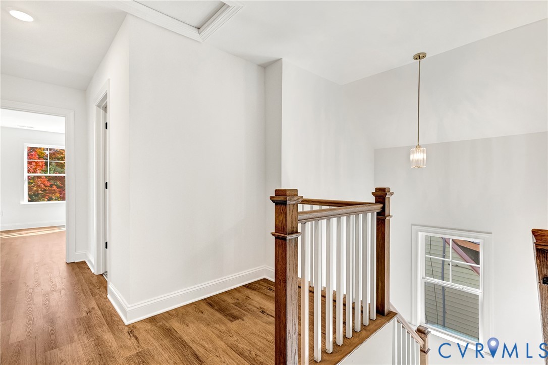 Landing area featuring wood-finish flooring, a classic staircase with a wood handrail, white balusters, multi-pane windows, and a singular pendant light fixture