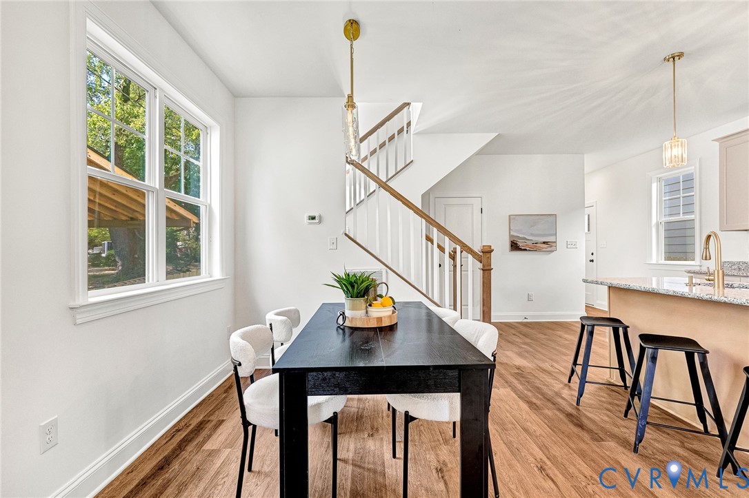 Wood-finish flooring throughout, staircase with wood handrail, kitchen island with stone-surface countertop, and hanging pendant lighting