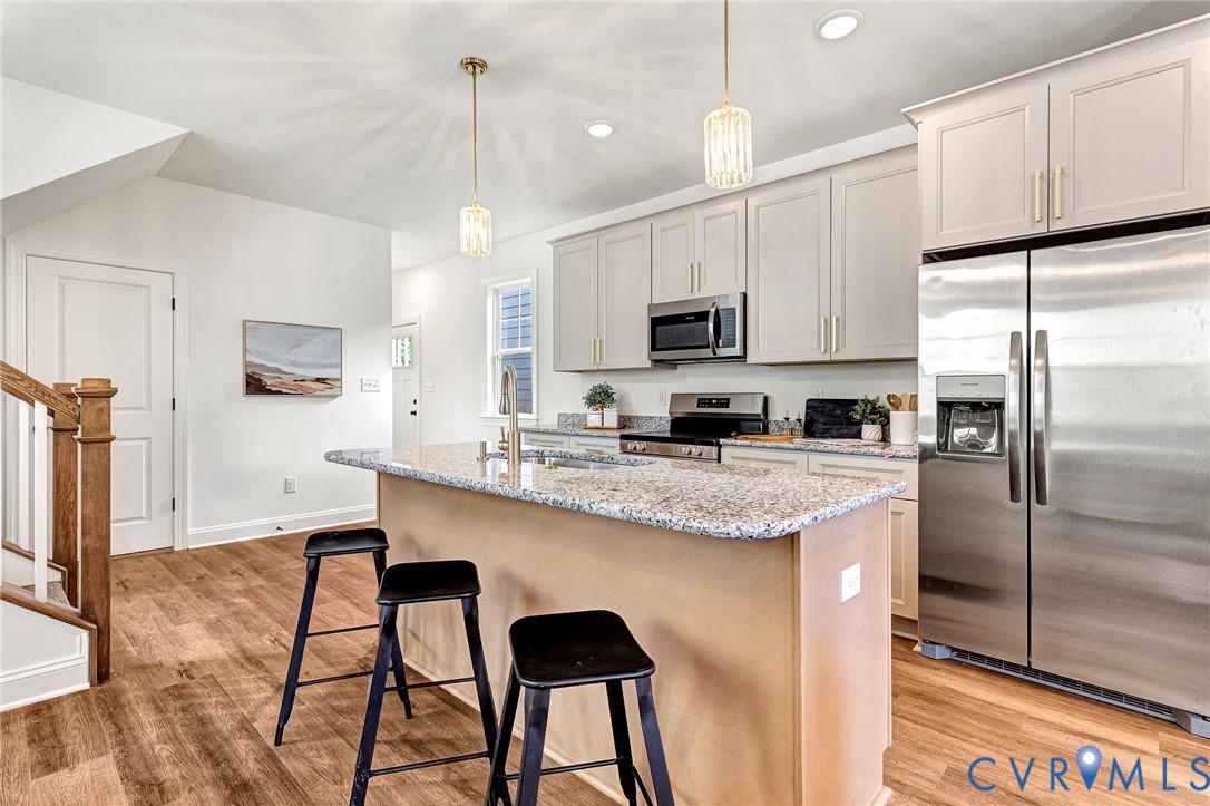 Kitchen featuring a center island with stone-finish countertops, stainless steel appliances, shaker-style cabinetry, and wood-finish flooring