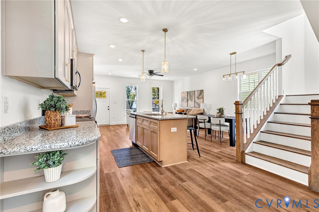 Kitchen featuring a central island with stone-style countertops, light-finish cabinetry, wood-finish flooring, recessed lighting, and a staircase with a wooden handrail and white balusters