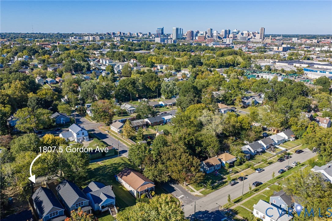 Aerial perspective featuring a residential property with a gabled roofline, mature trees, and a cityscape skyline in the distance