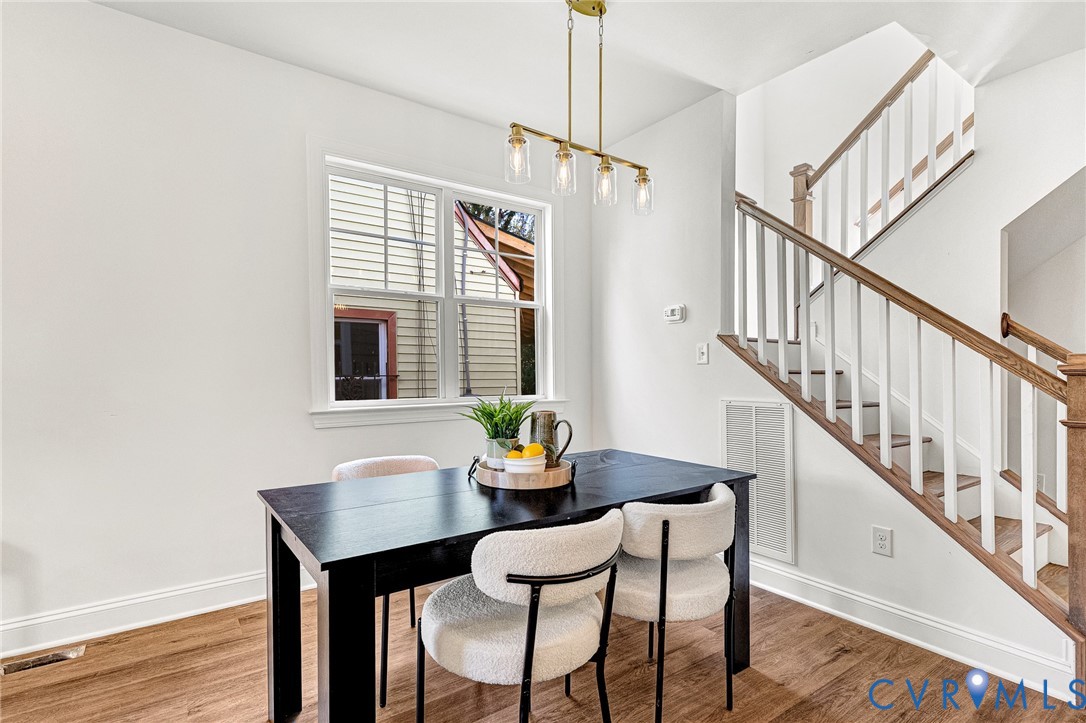 Staircase featuring white balusters and a wood-finish handrail, complemented by linear multi-light pendant lighting and wood-finish flooring