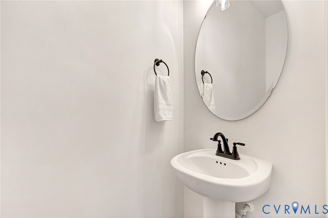 Pedestal sink with a dark-finish widespread faucet, oval mirror, and circular towel ring