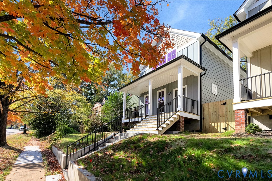 Elevated residence featuring vertical board-and-batten siding, a covered front porch with black metal railings, and concrete entry stairs