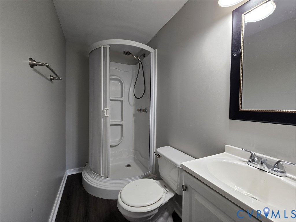 Corner shower unit with integrated shelving, vanity cabinet with basin sink, chrome faucet hardware, and wood-finish flooring
