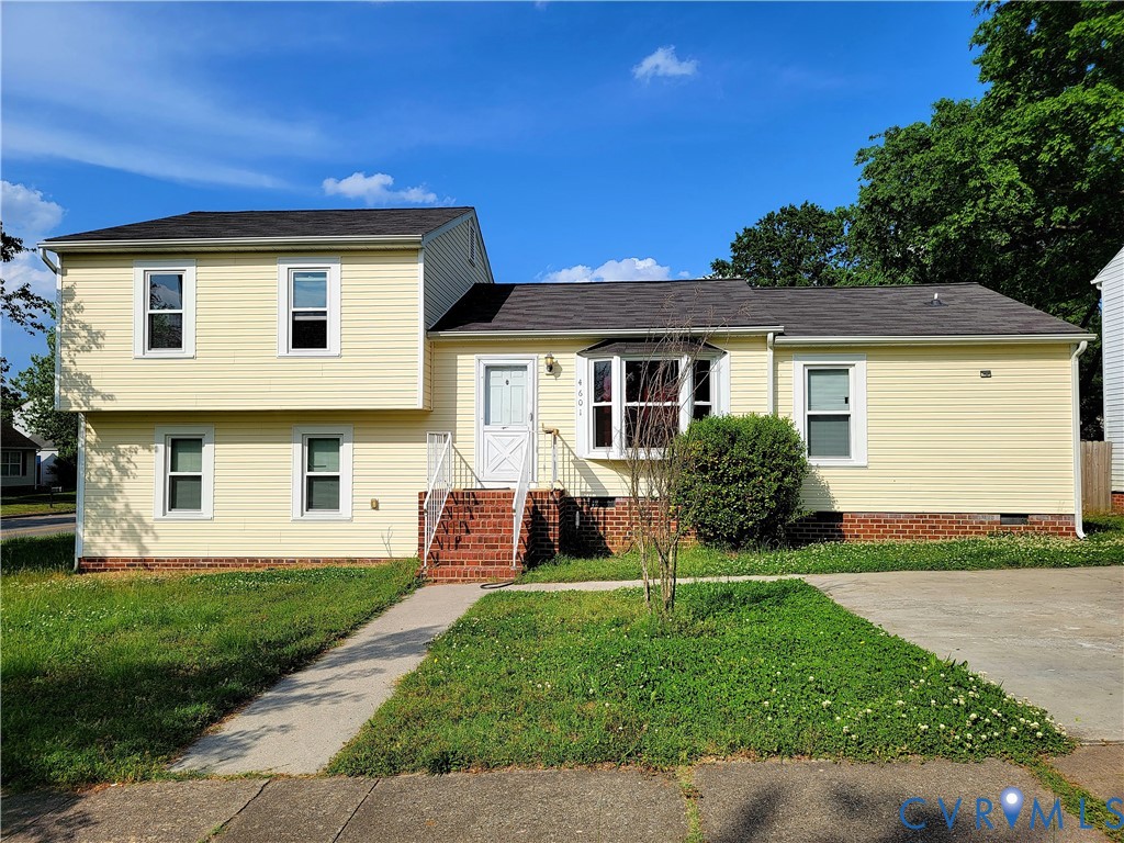 Split-level exterior featuring yellow horizontal siding, a brick foundation, a front-facing bay window, and a concrete driveway