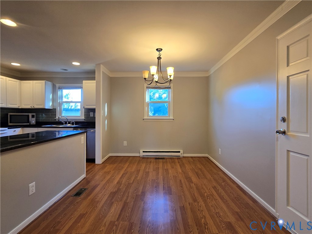 Wood-finish flooring, white cabinetry, dark countertops, crown molding, and a multi-arm chandelier