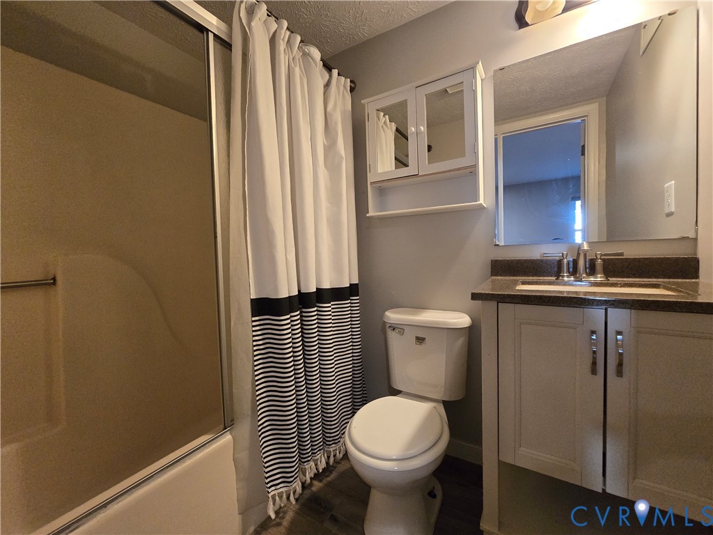 Bathroom featuring a vanity with a solid-surface countertop, an integrated sink, a wall-mounted mirrored medicine cabinet, a full-width mirror, and a tub-shower combination with a sliding glass enclosure