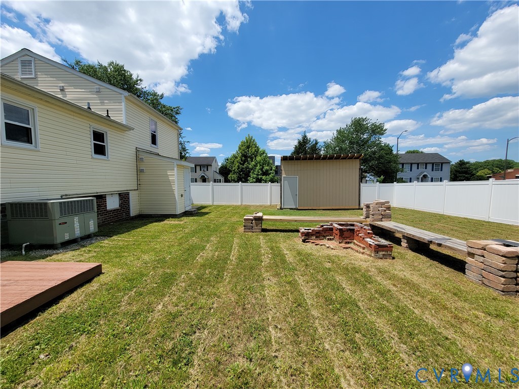 Fenced backyard featuring a brick fire pit, built-in masonry seating, a detached storage structure, and a wood-finish deck