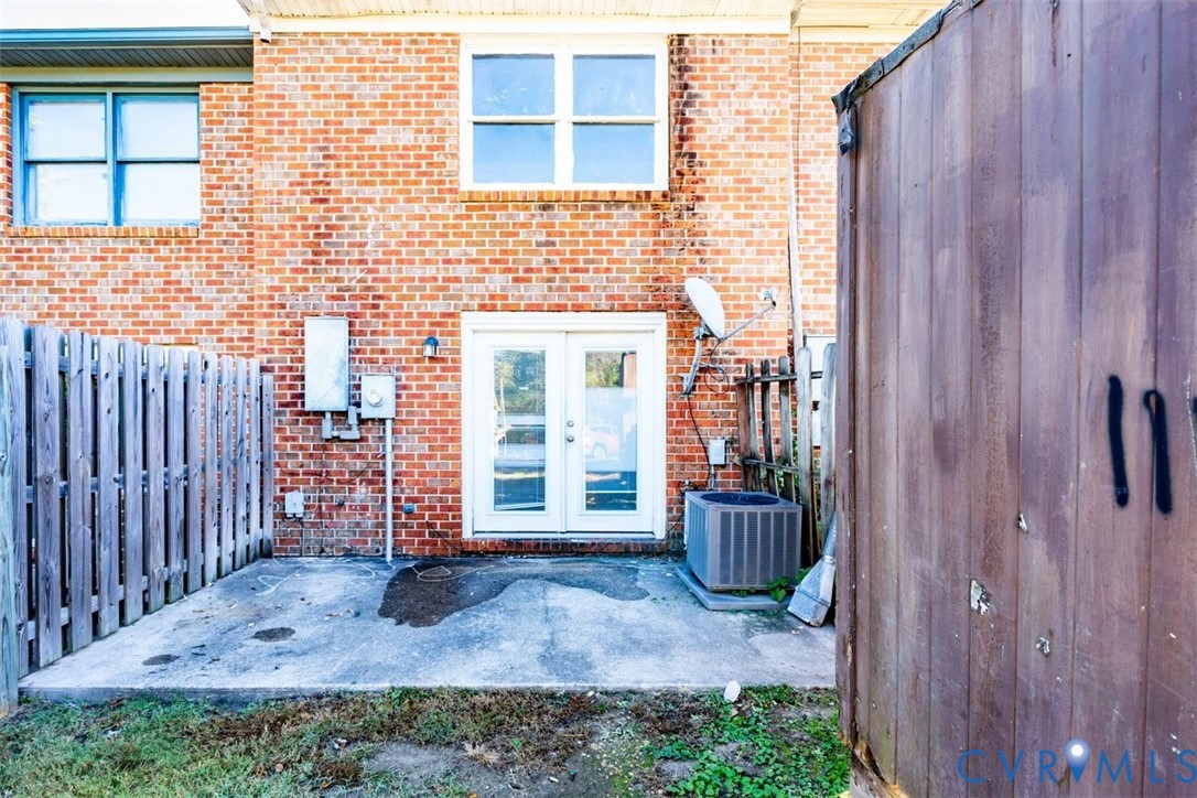 Exterior red brick facade featuring a concrete patio, white-framed French doors, and wood-style privacy fencing