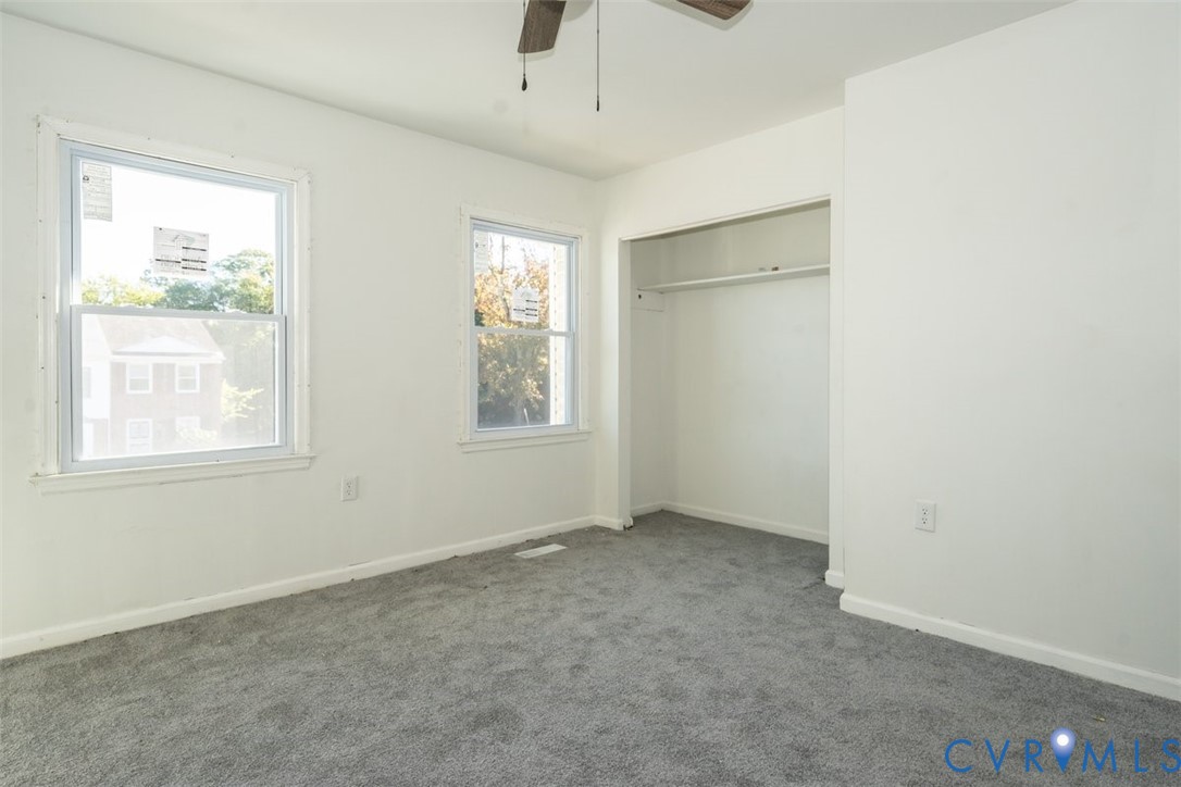 Neutral-toned interior space featuring wall-to-wall carpeting, dual-pane windows, a recessed closet with overhead shelving, and a ceiling fan